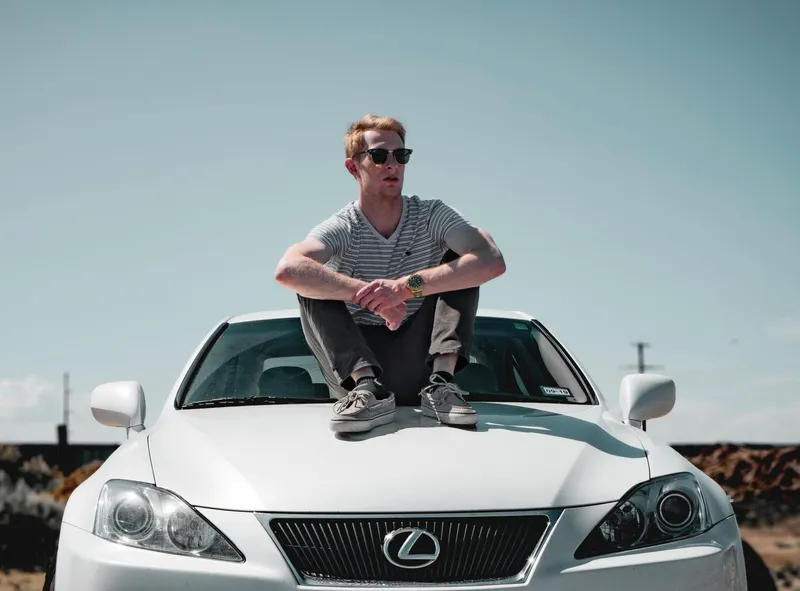 Чоловік сидить на капоті автоиобіля Lexus